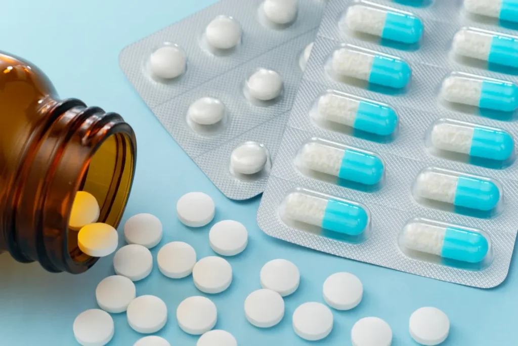 青い背景にカプセル薬と薬瓶からこぼれた錠剤の画像