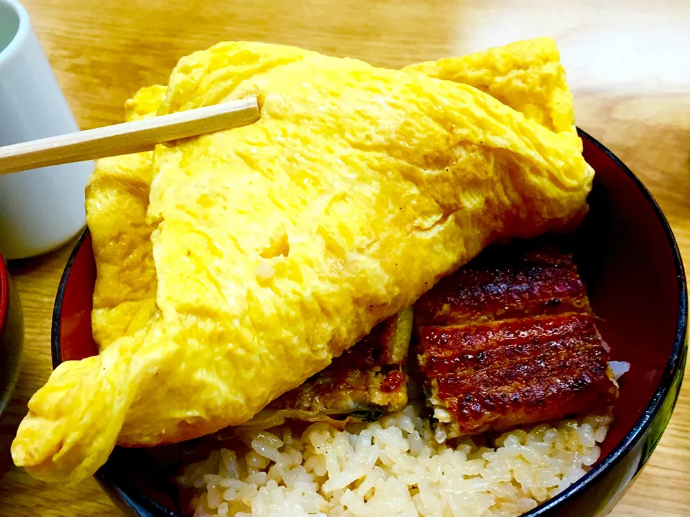 きんし丼のだし巻き卵を箸で持ち上げ、その下から鰻の蒲焼が見えている画像