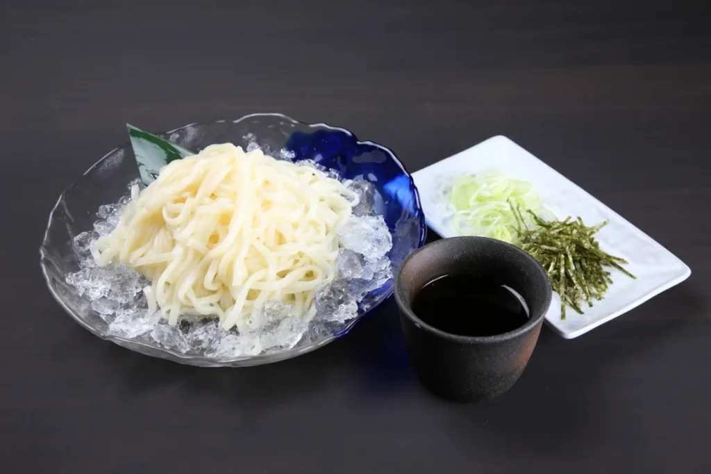 氷の上にのった冷たい稲庭うどんと薬味の画像