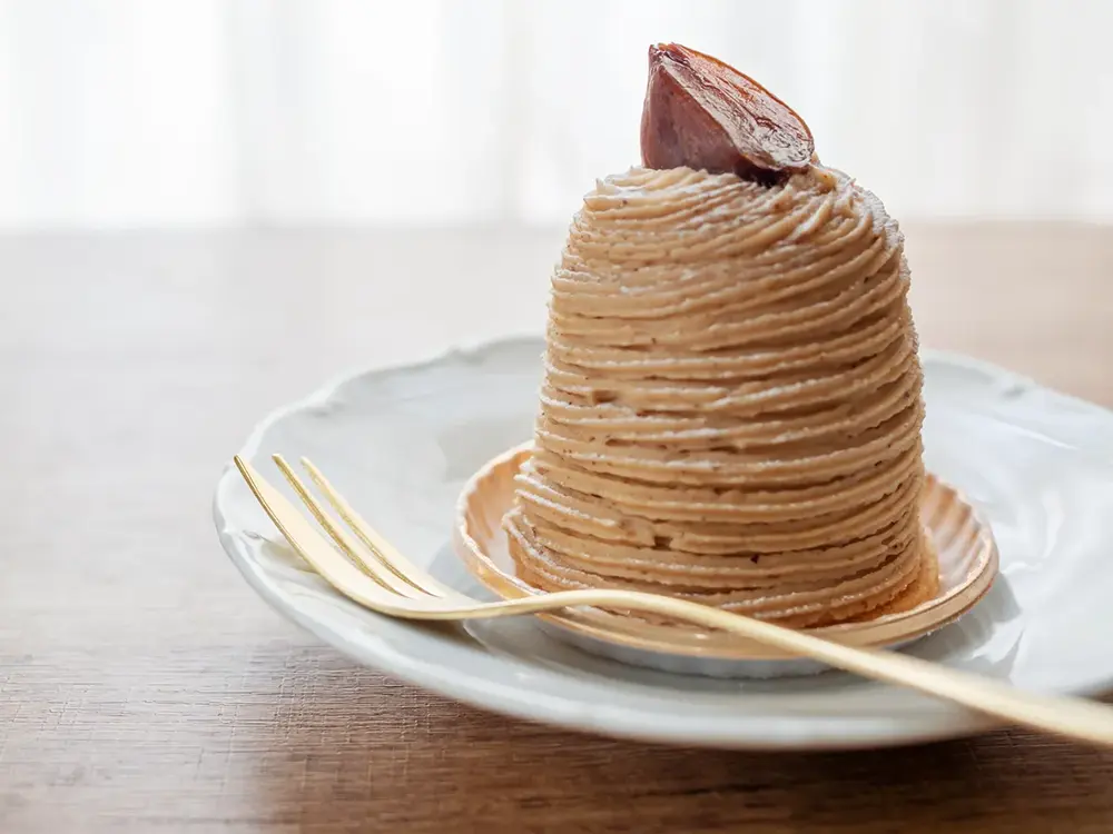 皿の上に置かれたモンブランのケーキとフォークの画像