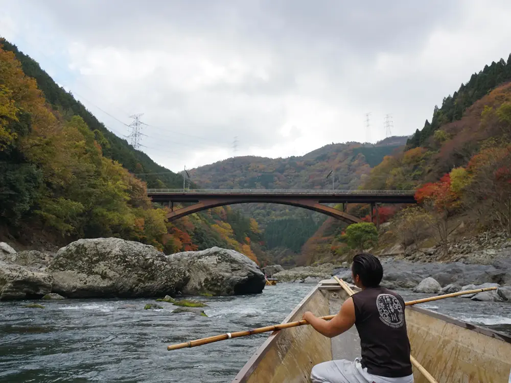 保津川下りの船上から見た船頭と鉄橋が見える景色の画像