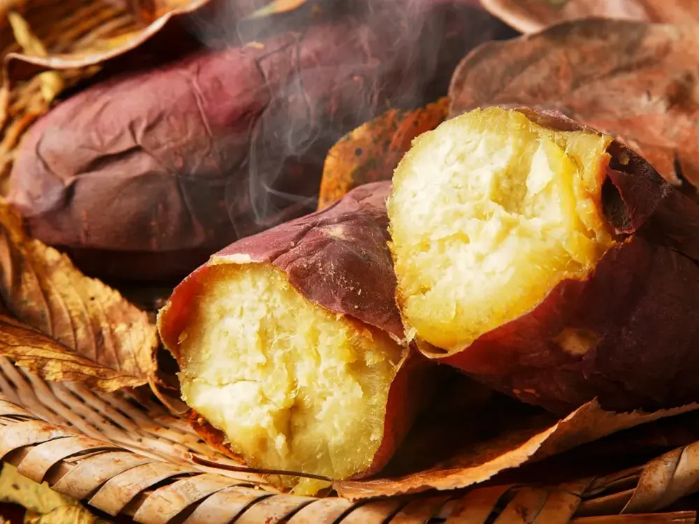 かごの中で湯気を立てる焼きたての焼き芋の画像