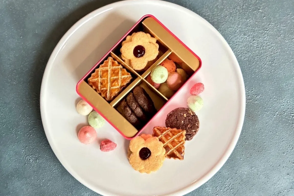 白い大皿に缶に入った「ビスキュイ・キャトル・アニヴェルセル」をのせ、缶の周りに4種類のクッキーを飾った画像