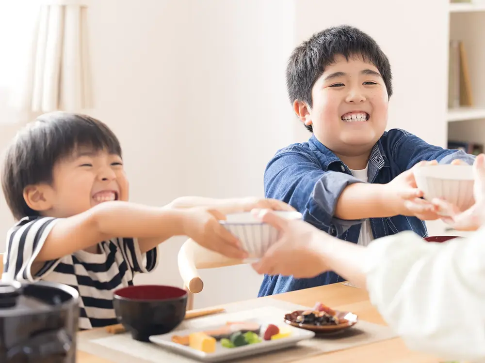 子供が笑顔でご飯茶碗を受け取っている食卓の画像
