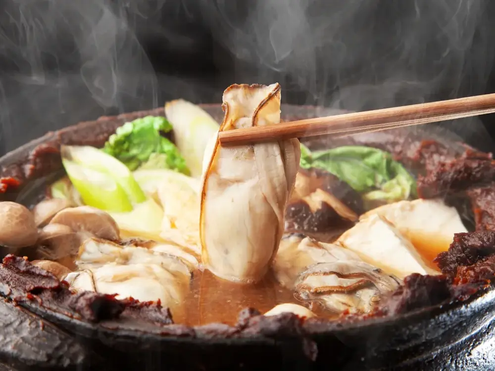 煮えているかきの土手鍋から牡蠣を持ち上げている画像