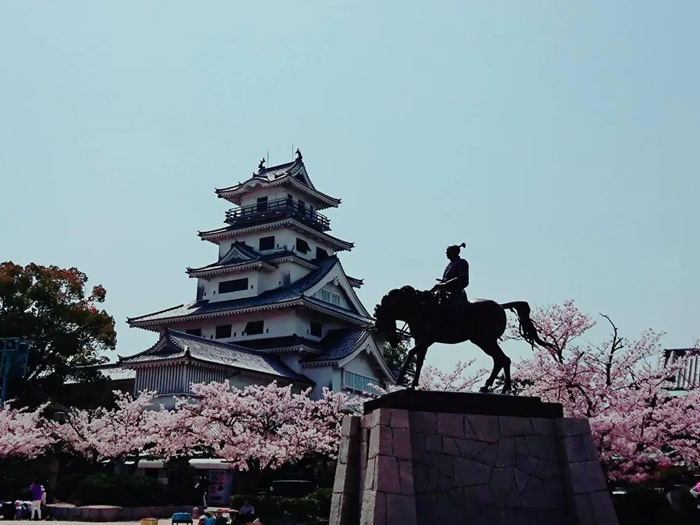 今治城天守閣をバックに桜の中に立つ藤堂高虎の像の画像