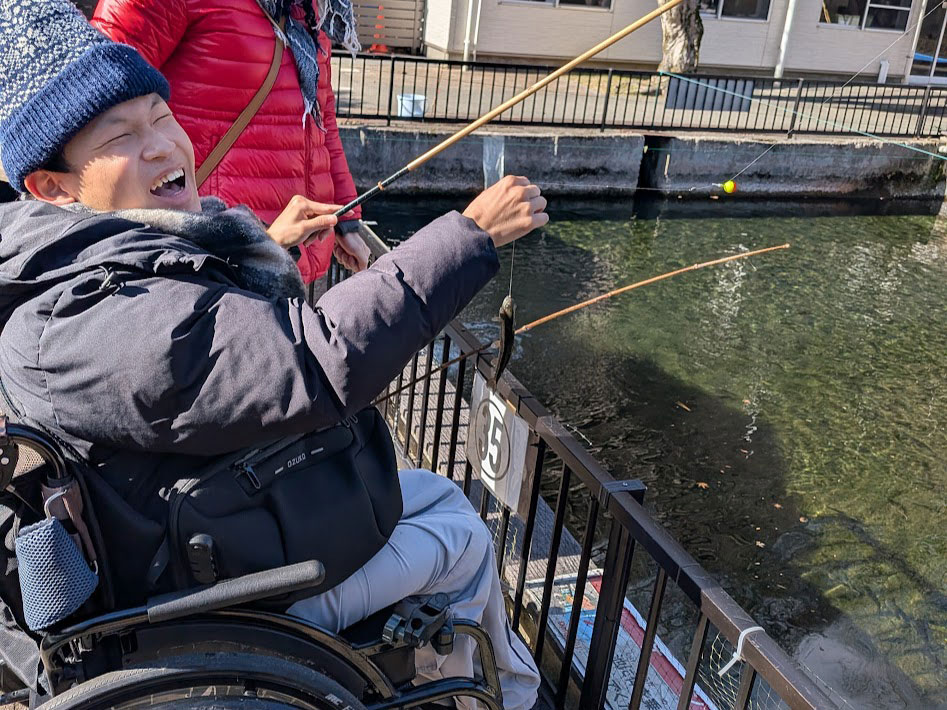 釣り堀で釣りを楽しむ笑顔の車椅子ユーザーの男性の画像