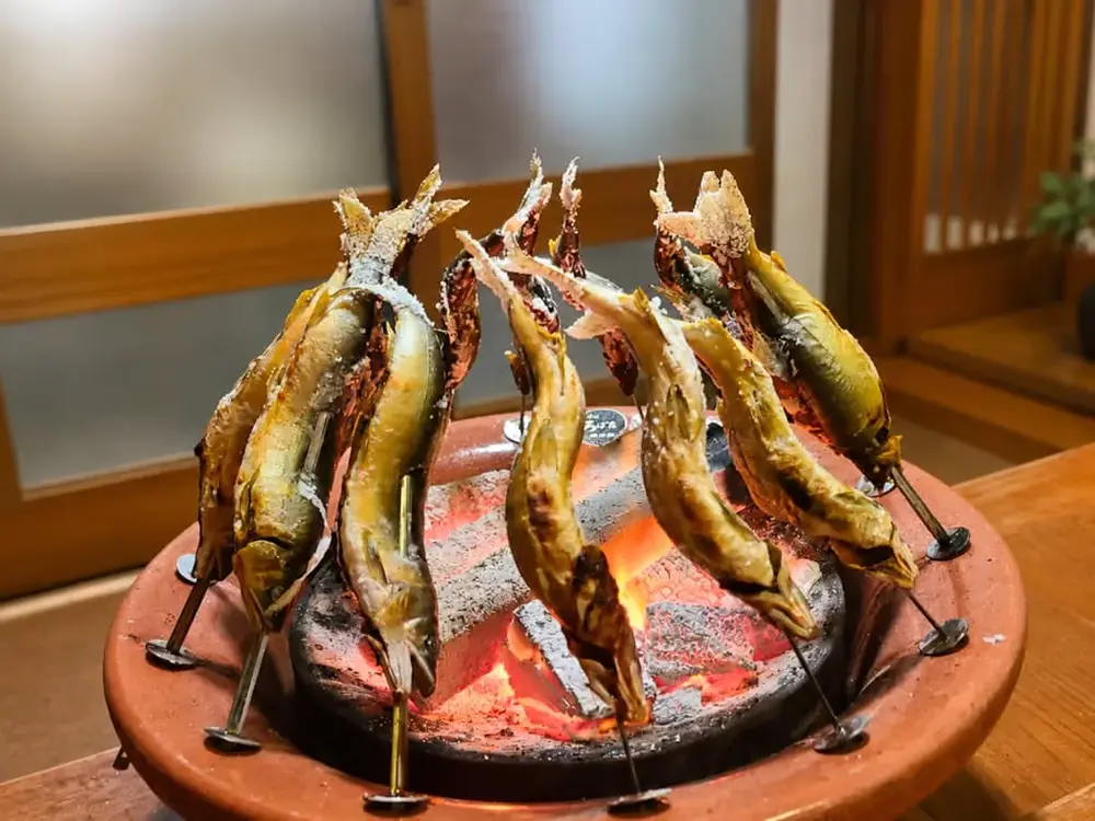 鮎を串に刺し、炭火焼きしている画像