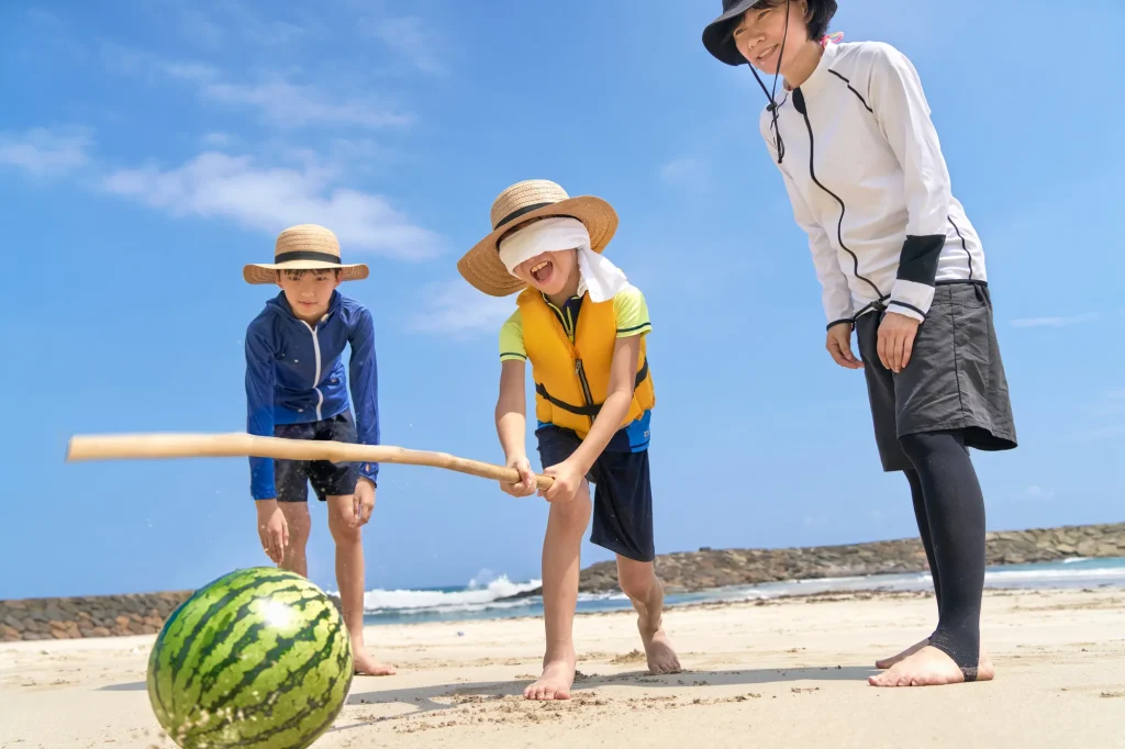 夏の海辺でスイカ割りを楽しむ家族の画像